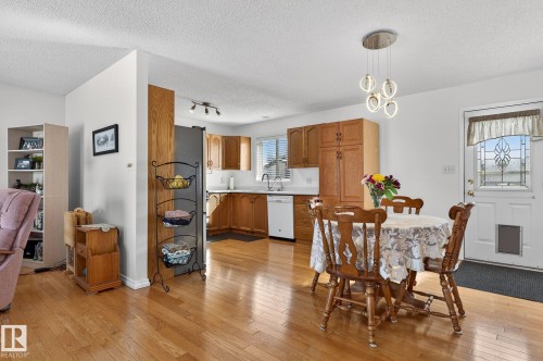 The property features hardwood floors throughout, a kitchen with wood cabinetry and white appliances, and a dining area with a modern light fixture - 22 Riverpointe, Fort Saskatchewan, AB - Indoor Photo Showing Dining Room