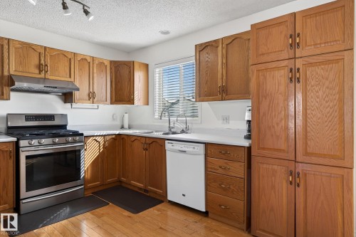 The kitchen features wood cabinetry, a stainless steel range with overhead ventilation, and a white dishwasher - 22 Riverpointe, Fort Saskatchewan, AB - Indoor Photo Showing Kitchen With Double Sink
