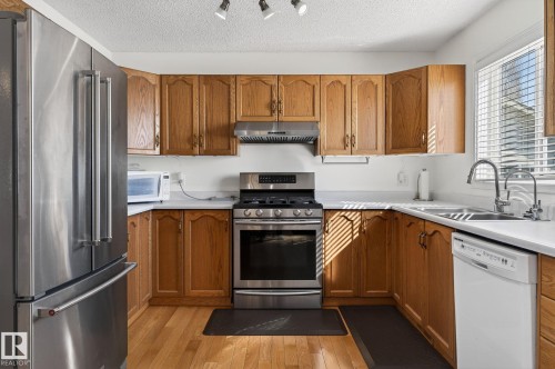 The kitchen features wood cabinetry, white countertops, stainless steel appliances, and wood flooring - 22 Riverpointe, Fort Saskatchewan, AB - Indoor Photo Showing Kitchen With Double Sink