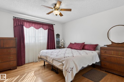 The room features light hardwood flooring, a ceiling fan with integrated lighting, and a large window with privacy blinds and decorative drapes - 22 Riverpointe, Fort Saskatchewan, AB - Indoor Photo Showing Bedroom