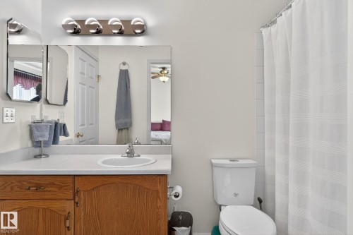 The bathroom features a light-colored vanity countertop with an integrated sink, wooden cabinetry with brass hardware, and a large mirror with overhead lighting - 22 Riverpointe, Fort Saskatchewan, AB - Indoor Photo Showing Bathroom