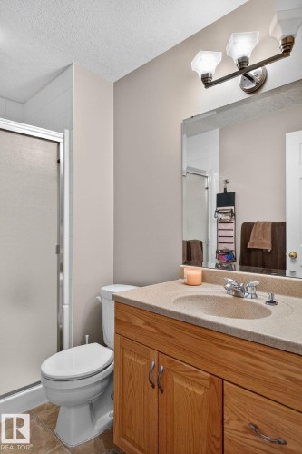 Bathroom featuring a light wood vanity with a solid surface countertop and an integrated sink, a large mirror, and a shower with a sliding glass door - 22 Riverpointe, Fort Saskatchewan, AB - Indoor Photo Showing Bathroom