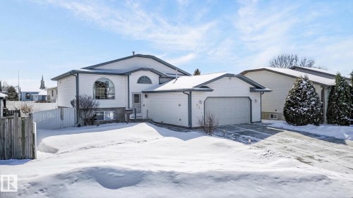 The property features a white exterior with a contrasting dark roof trim, an arched window, and an integrated garage with a driveway - 22 Riverpointe, Fort Saskatchewan, AB - Outdoor