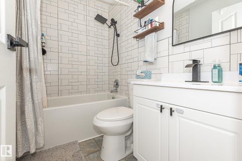 Bathroom featuring white subway tile with dark grout, a modern black shower head, a white vanity with white countertop, and a contemporary black faucet - 8326 157 Avenue, Edmonton, AB - Indoor Photo Showing Bathroom