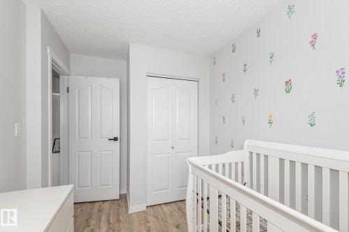 This room features hardwood-style flooring, a white bi-fold closet door, and a white interior door with dark hardware - 8326 157 Avenue, Edmonton, AB - Indoor