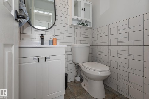 The bathroom features a vanity with a white countertop and a contemporary black faucet, complemented by a round black-framed mirror - 8326 157 Avenue, Edmonton, AB - Indoor Photo Showing Bathroom