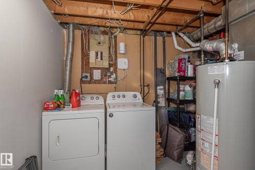 This utility area features a washing machine and dryer, a water heater, and exposed ceiling joists - 8326 157 Avenue, Edmonton, AB - Indoor
