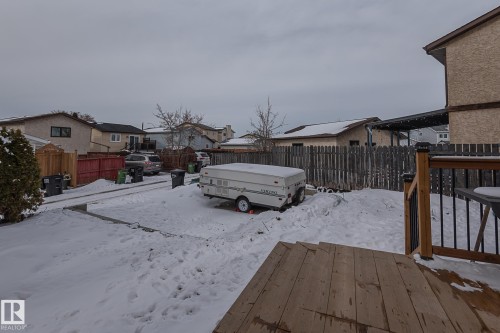 The property includes a wooden deck with black railings, a spacious snow-covered yard, and a paved driveway - 8326 157 Avenue, Edmonton, AB - Outdoor With Exterior