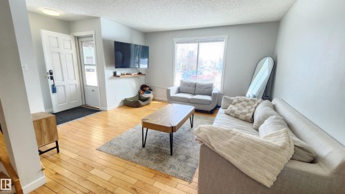The living area features hardwood flooring, a large window providing natural light, and a clean, light-colored wall finish - 8326 157 Avenue, Edmonton, AB - Indoor Photo Showing Living Room