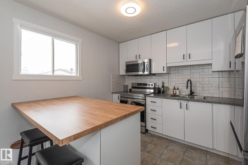The kitchen features white cabinetry, stainless steel appliances, a grey subway tile backsplash, and dark granite countertops - 8326 157 Avenue, Edmonton, AB - Indoor Photo Showing Kitchen With Double Sink