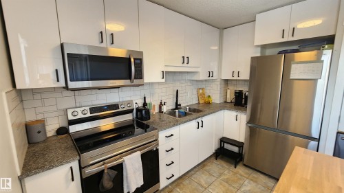 The kitchen features white cabinetry with black hardware, granite countertops, and stainless steel appliances including a refrigerator, range, and microwave - 8326 157 Avenue, Edmonton, AB - Indoor Photo Showing Kitchen With Double Sink With Upgraded Kitchen