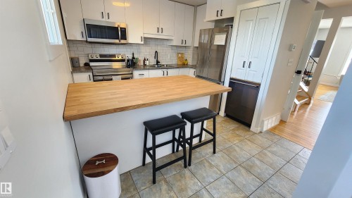 The kitchen features white cabinetry, a light wood countertop on the island, and stainless steel appliances - 8326 157 Avenue, Edmonton, AB - Indoor Photo Showing Kitchen