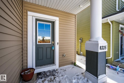 The property features a front door with a window pane, framed by white trim and tan siding - 8225 24 Avenue, Edmonton, AB - Outdoor With Deck Patio Veranda With Exterior