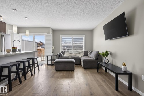 Open concept living area featuring hardwood flooring, a kitchen island with seating, and a large sliding glass door - 8225 24 Avenue, Edmonton, AB - Indoor Photo Showing Living Room