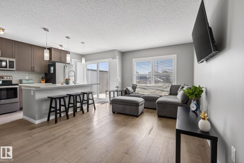 Open concept living space featuring hardwood floors, a kitchen island with seating, stainless steel appliances, and sliding glass doors - 8225 24 Avenue, Edmonton, AB - Indoor