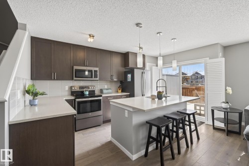 The kitchen features dark wood cabinetry, stainless steel appliances, light-colored countertops, and a kitchen island with pendant lighting - 8225 24 Avenue, Edmonton, AB - Indoor Photo Showing Kitchen With Upgraded Kitchen