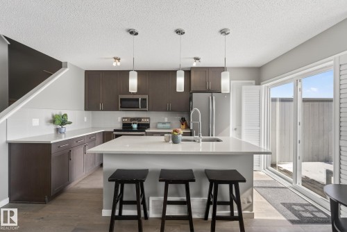The kitchen features dark wood cabinetry, stainless steel appliances, and a central island with a sink and pendant lighting - 8225 24 Avenue, Edmonton, AB - Indoor Photo Showing Kitchen With Upgraded Kitchen