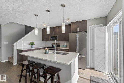 The kitchen features a spacious island with a light-colored countertop, dark wood cabinetry, stainless steel appliances, and a white subway tile backsplash - 8225 24 Avenue, Edmonton, AB - Indoor Photo Showing Kitchen With Upgraded Kitchen