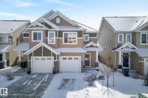 The property features a two-story design with a combination of tan and dark green siding, white trim, and a snow-covered roof - 8225 24 Avenue, Edmonton, AB - Outdoor With Facade