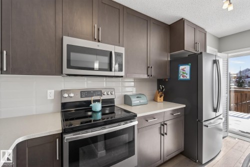 The kitchen features dark wood cabinetry, light-colored countertops, and stainless steel appliances including a microwave, range, and refrigerator - 8225 24 Avenue, Edmonton, AB - Indoor Photo Showing Kitchen