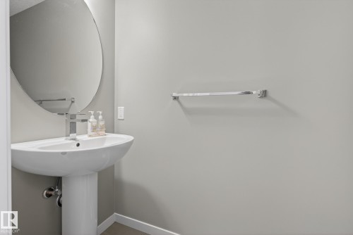 Bathroom featuring a pedestal sink with a modern faucet and a round wall mirror - 8225 24 Avenue, Edmonton, AB - Indoor Photo Showing Bathroom