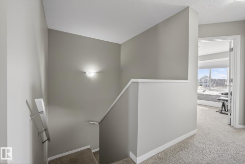 Carpeted stairs with a wall-mounted light fixture lead to a landing with a doorway, revealing an interior space with large windows - 8225 24 Avenue, Edmonton, AB - Indoor Photo Showing Other Room