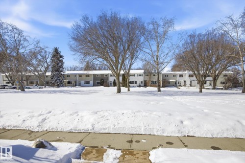 The property features a multi-unit residential building with light-colored siding and a contrasting roofline, set amidst mature trees - 6 Garden Crescent, St. Albert, AB - Outdoor