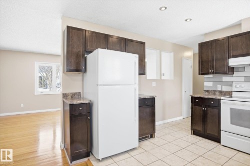 The kitchen features dark wood cabinetry, a white refrigerator, and white tile flooring - 6 Garden Crescent, St. Albert, AB - Indoor Photo Showing Kitchen