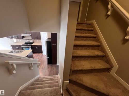 Carpeted stairs with white handrails and a view of the kitchen featuring dark wood cabinetry, a stainless steel range, and an island with a sink - 1421 26 Avenue, Edmonton, AB - Indoor Photo Showing Other Room