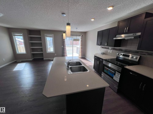The property features a kitchen with dark cabinetry, stainless steel appliances, and a central island with a double sink - 1421 26 Avenue, Edmonton, AB - Indoor Photo Showing Kitchen With Stainless Steel Kitchen With Double Sink