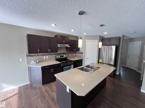 The kitchen features dark wood cabinetry, a light-colored island with an integrated double sink, stainless steel appliances, and pendant lighting - 1421 26 Avenue, Edmonton, AB - Indoor Photo Showing Kitchen With Stainless Steel Kitchen With Double Sink With Upgraded Kitchen