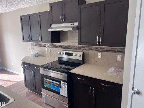 The kitchen features dark wood cabinetry, light-colored countertops, a tile backsplash, and stainless steel appliances including a range and range hood - 1421 26 Avenue, Edmonton, AB - Indoor Photo Showing Kitchen With Stainless Steel Kitchen With Upgraded Kitchen