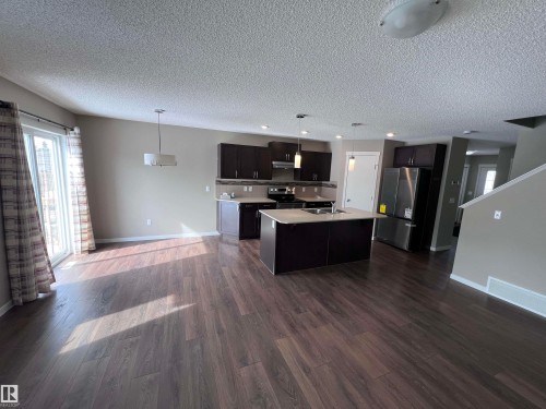 Spacious open concept living area featuring dark wood flooring, a kitchen island with a sink, and a patio door providing natural light - 1421 26 Avenue, Edmonton, AB - Indoor Photo Showing Kitchen