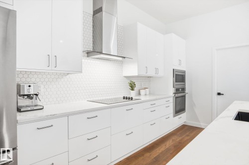 Modern kitchen featuring white cabinetry, a hexagonal tiled backsplash, stainless steel appliances, and wood flooring - 9821 85 Avenue, Edmonton, AB - Indoor Photo Showing Kitchen With Upgraded Kitchen