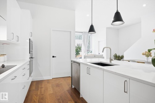 Modern kitchen featuring white cabinetry, light-colored countertops, and hardwood flooring - 9821 85 Avenue, Edmonton, AB - Indoor Photo Showing Kitchen With Upgraded Kitchen