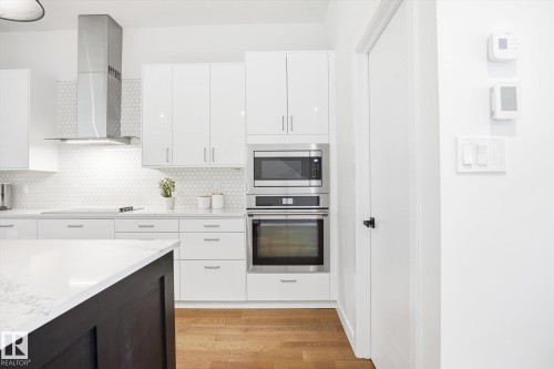 Well-appointed kitchen featuring white cabinetry, stainless steel appliances, a white hexagonal tile backsplash, and a dark island with a light-colored countertop - 9821 85 Avenue, Edmonton, AB - Indoor Photo Showing Kitchen With Upgraded Kitchen
