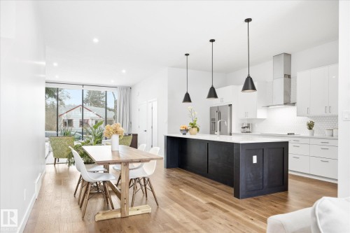 Open-concept living area featuring hardwood flooring, a modern kitchen with a large island and pendant lighting, and full-height windows providing natural light - 9821 85 Avenue, Edmonton, AB - Indoor