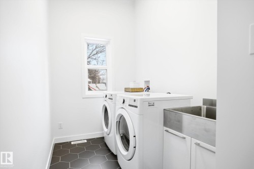 Utility area featuring hexagonal floor tiles, a window providing natural light, a stainless steel sink, and white cabinetry - 9821 85 Avenue, Edmonton, AB - Indoor Photo Showing Laundry Room