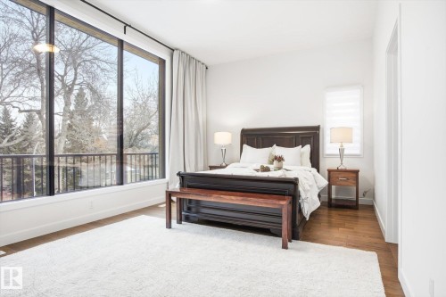 This room features expansive floor-to-ceiling windows, a dark wood bed frame, and light hardwood flooring - 9821 85 Avenue, Edmonton, AB - Indoor Photo Showing Bedroom