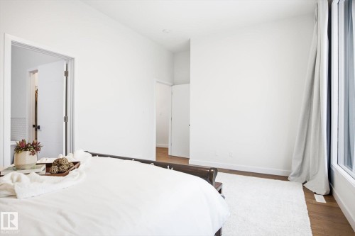 This inviting room features light-colored walls, a large window with drapes, and wood flooring - 9821 85 Avenue, Edmonton, AB - Indoor Photo Showing Bedroom