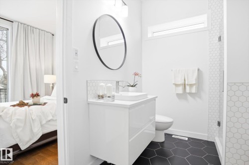 The bathroom features a modern floating vanity with a vessel sink, a toilet, and black hexagonal floor tiles - 9821 85 Avenue, Edmonton, AB - Indoor Photo Showing Bathroom