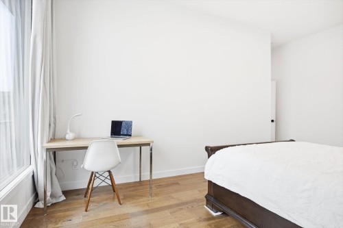 This room features light-toned hardwood flooring, white walls, and a window with light-colored curtains - 9821 85 Avenue, Edmonton, AB - Indoor