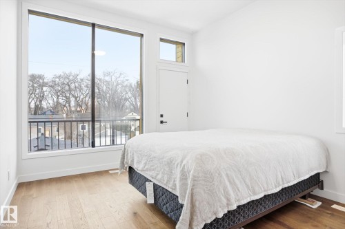 This room features expansive windows, a door leading to a balcony with a black metal railing, and light-colored hardwood flooring - 9821 85 Avenue, Edmonton, AB - Indoor Photo Showing Bedroom