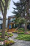 AI generated with summer flowers and shrubs, which are for illustration purposes only. The property features a contemporary exterior with a dark facade and warm wood accents, complemented by two distinctive blue entry doors - 9821 85 Avenue, Edmonton, AB  - Outdoor With Deck Patio Veranda 
