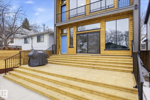 The property features an extensive wooden deck with stairs, black railings, and a sliding glass door leading into the interior - 9821 85 Avenue, Edmonton, AB - Outdoor With Exterior