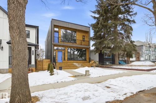 The property features a contemporary exterior with wood siding and large windows, complemented by a vibrant blue front door and a matching blue balcony door - 9821 85 Avenue, Edmonton, AB - Outdoor With Facade