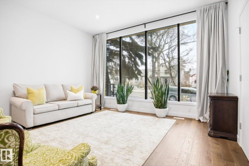 Living area featuring hardwood flooring, a large area rug, and a full-height picture window with curtain rods and drapes - 9821 85 Avenue, Edmonton, AB - Indoor