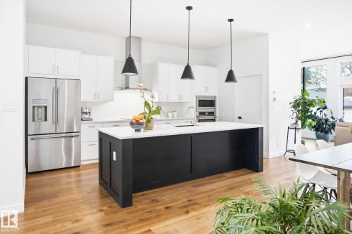 Well-appointed kitchen featuring a large island with a white countertop, modern pendant lighting, white cabinetry, and stainless steel appliances - 9821 85 Avenue, Edmonton, AB - Indoor Photo Showing Kitchen With Stainless Steel Kitchen With Upgraded Kitchen