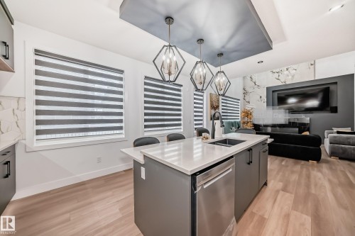Open concept living space featuring a kitchen island with a sink and a dishwasher, hardwood flooring, and a living area with a dark accent wall - 15108 11 Street, Edmonton, AB - Indoor Photo Showing Kitchen