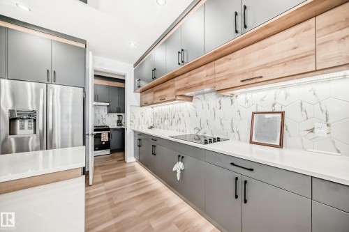 Modern kitchen featuring grey and wood-toned cabinetry, stainless steel appliances, white countertops, and a geometric tile backsplash - 15108 11 Street, Edmonton, AB - Indoor Photo Showing Kitchen With Upgraded Kitchen